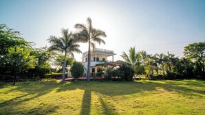 A two-story house with a balcony, surrounded by a well-maintained lawn and palm trees. - JAWAI INTO THE WILD (Bali)