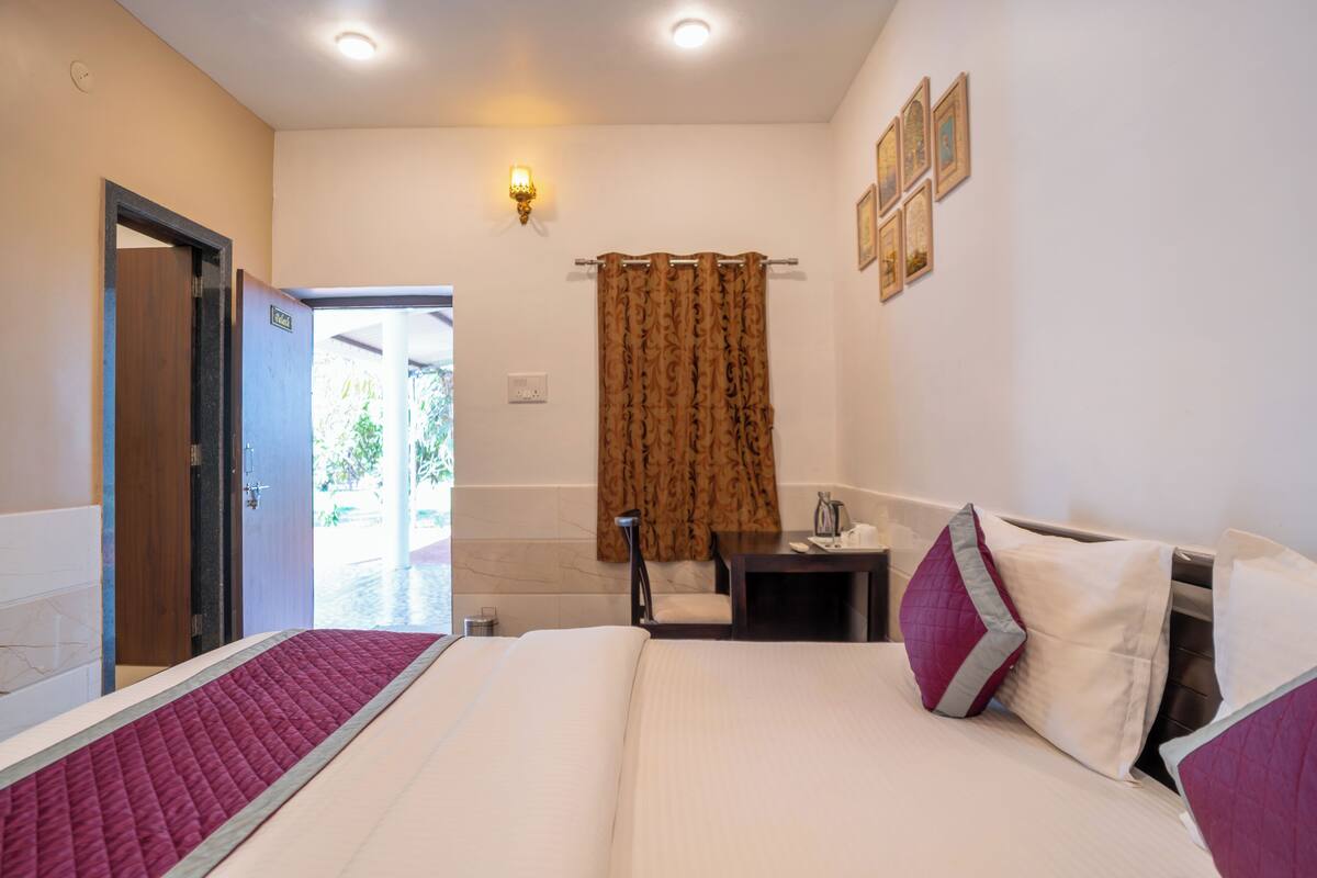 A hotel room with a bed, a desk, a chair, a shower area, and a wall-mounted light.