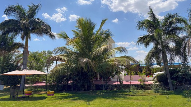 A lush garden with palm trees, a covered seating area, and a building with a red roof. - JAWAI INTO THE WILD (Bali)