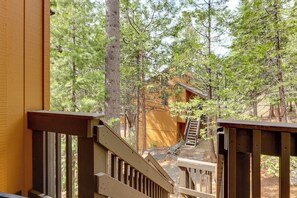 Eine Holzterrasse mit einer Treppe, die zu einer umgeben von Bäumen liegenden Hütte führt.