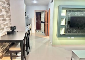 A modern kitchen with a coffee maker, a dining area with chairs, a TV mounted on a wall, and a door leading to another room. - Large condo middle of jomtien, near the beach 42m2 (Pattaya City)