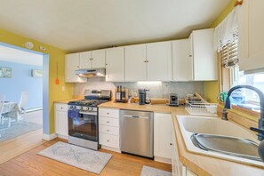 Una cucina compatta con mobili bianchi, fornelli, lavastoviglie e lavello.