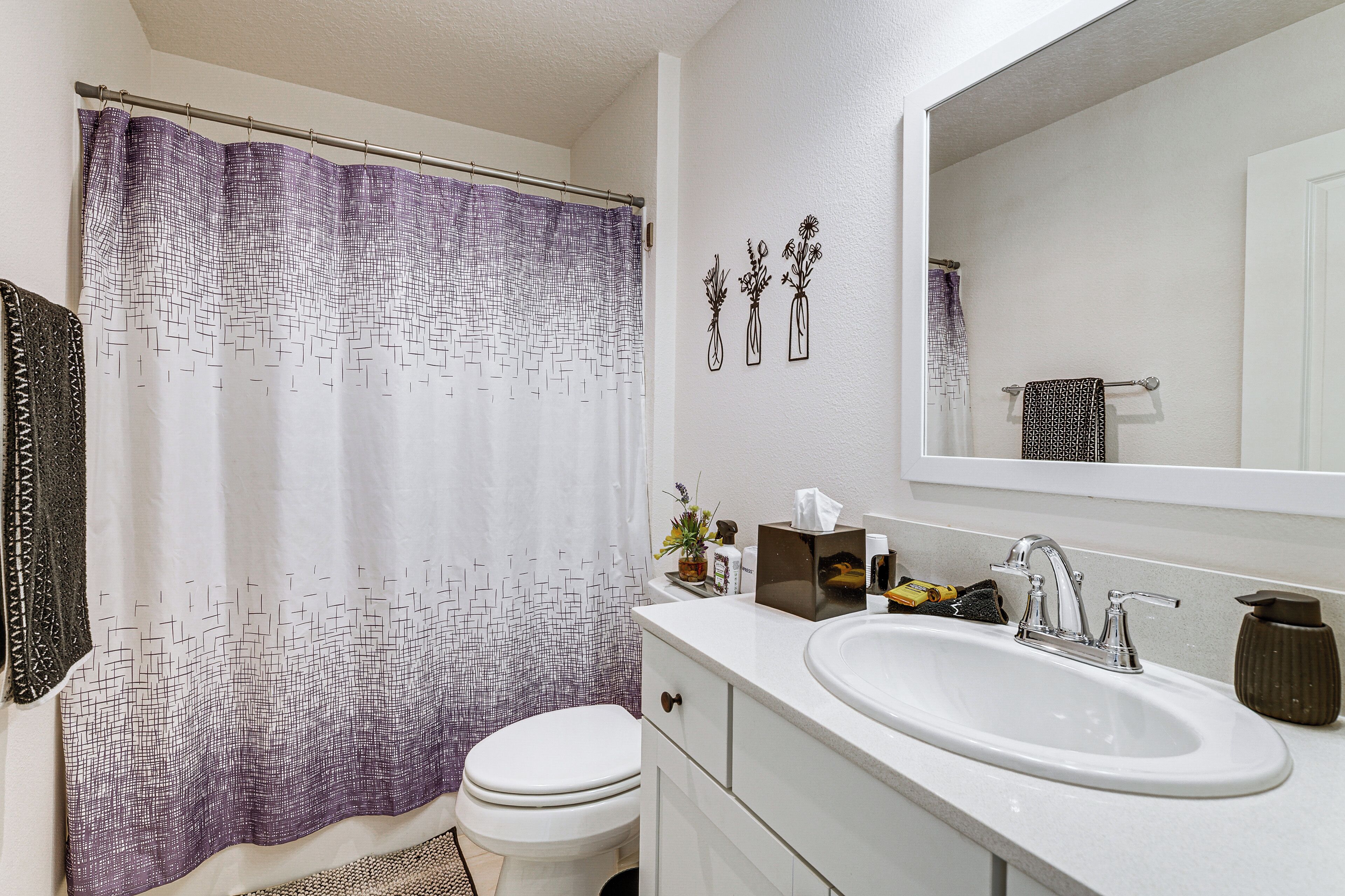 A bathroom with a shower curtain, toilet, sink, and mirror.