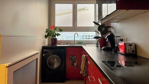 Eine kompakte Küche mit Waschmaschine, einem roten Schrank, einem Toaster und einem Fenster mit Blick auf eine Baustelle.
