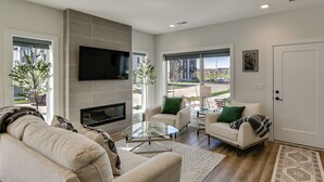 Een moderne woonkamer met een flatscreen televisie, een open haard, een bank, een salontafel en uitzicht op buiten.
