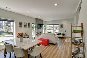 A modern living room with a dining area, a sofa, a red ottoman, and a TV mounted on the wall. - Rooftop Oasis: Downtown Des Moines Townhome (Des Moines)