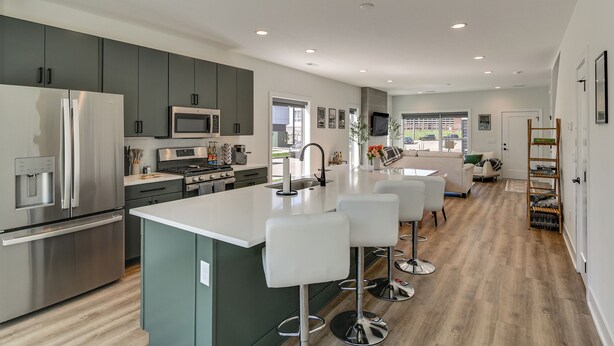Een moderne keuken met roestvrijstalen apparatuur, een centraal eiland met barstoelen en een zithoek met een witte bank en tafel.