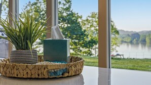 Ein Blumentopf, eine Seifenschale und ein gewebter Korb auf einem Tisch mit Blick auf einen See und Bäume.