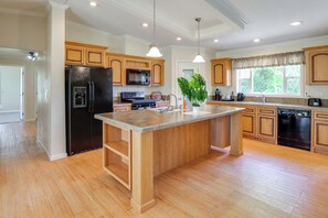 Une cuisine moderne avec des meubles en bois, un îlot central, des appareils électroménagers en acier inoxydable et des luminaires suspendus.