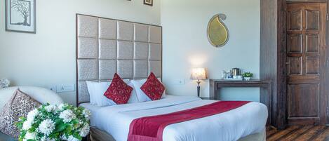 A hotel room with a large bed, a bedside table with a vase of flowers, a nightstand with a lamp, and a wooden wardrobe.