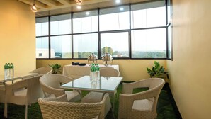Un salón de conferencias con una mesa de vidrio, sillas de mimbre, dos lámparas y vistas amplias a través de grandes ventanas.