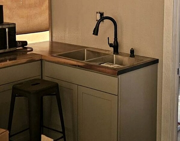 A compact kitchen with a single sink, a stool, and a microwave.