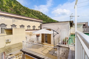 A balcony with a white umbrella, a staircase, and a view of a hillside.