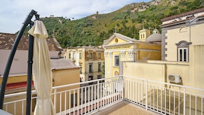Un balcón con baranda blanca, un edificio amarillo con cúpula y un cerro verde al fondo.