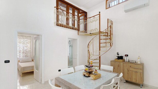 Un comedor con una mesa, sillas, una escalera, un armario de madera y una puerta que da a otra habitación.
