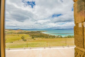A view from a balcony overlooking a coastal landscape with a body of water, grassy fields, and distant hills. - StayAU Pet-friendly Coastal&Bay Views w/fireplace (Carlton River)