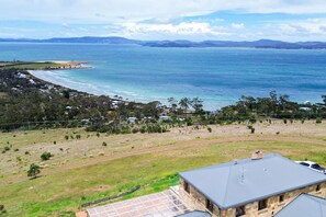 A coastal property with a large house, a view of the ocean, and a hilly landscape in the background. - StayAU Pet-friendly Coastal&Bay Views w/fireplace (Carlton River)