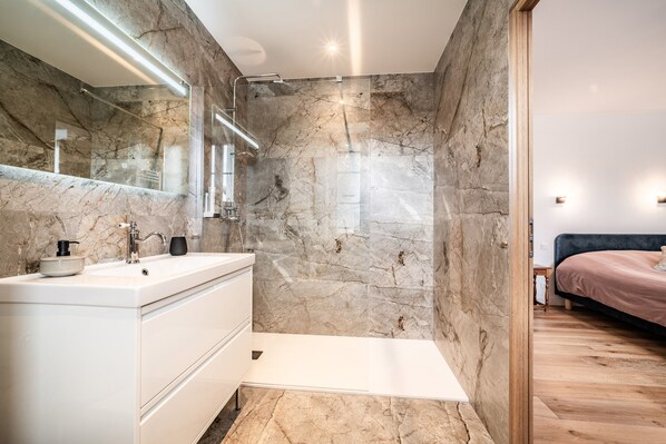 Un baño moderno con pared de mármol, tocador blanco y cabina de ducha de vidrio.