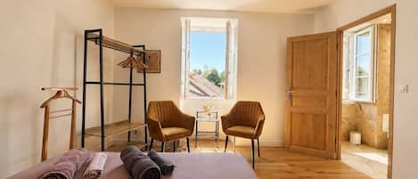 A bedroom with a bed, two chairs, a wooden wardrobe, a window, and a door.