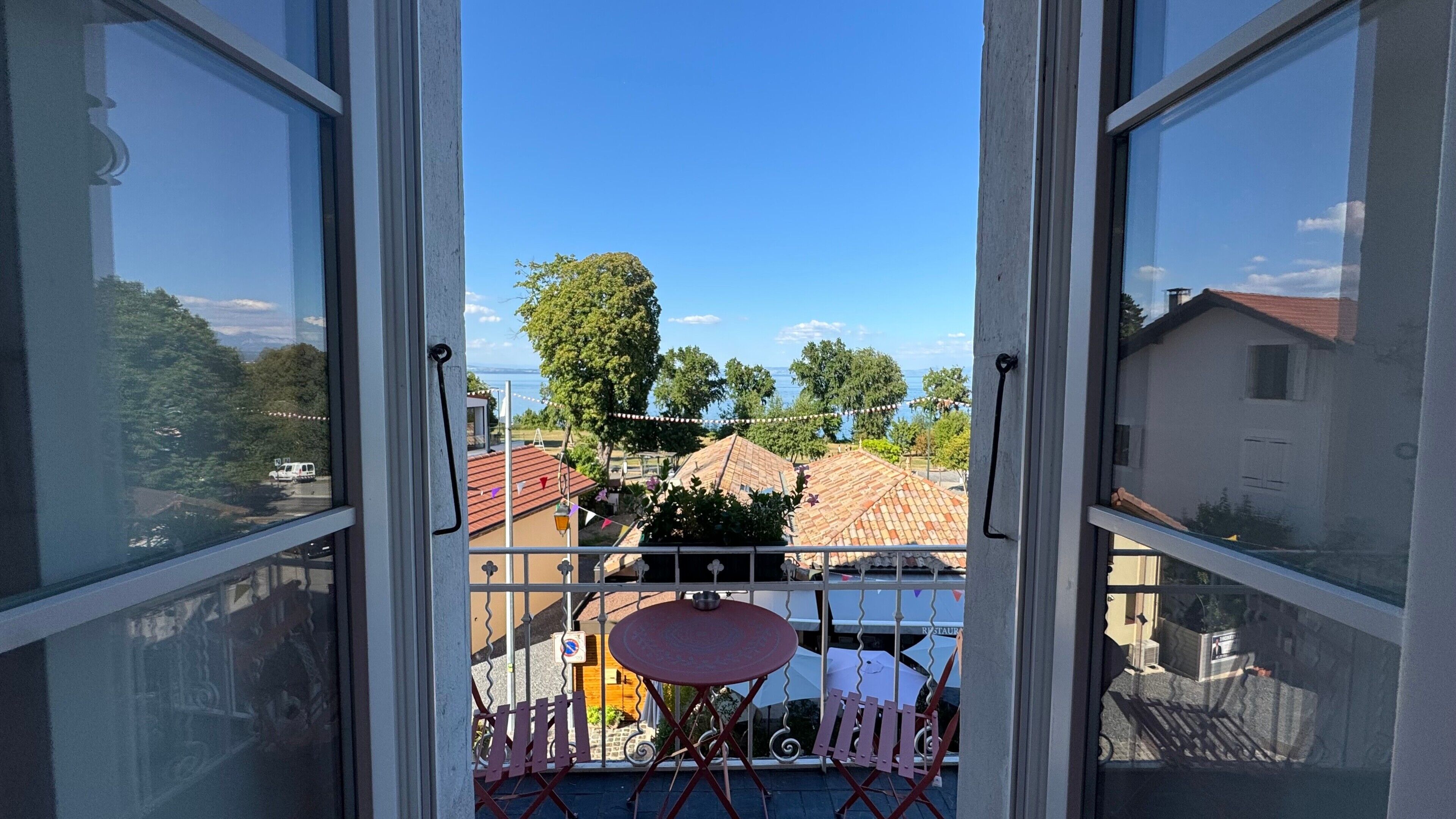 A balcony with a table and chairs, overlooking a residential area with houses and a clear sky.