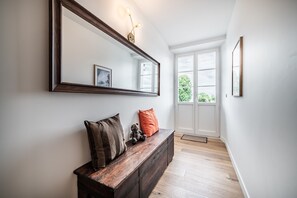 A hallway with a wooden bench, a large mirror, and a door leading to a bright room with a window.
