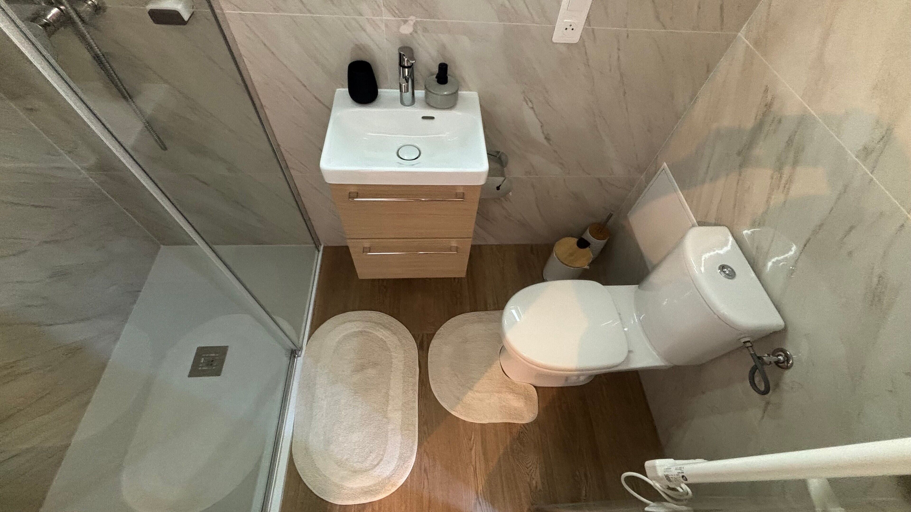 Une salle de bain avec douche, toilettes, lavabo et tapis en bois.