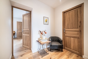 Un couloir avec des portes en bois, une petite table sur laquelle est posé un vase, et un fauteuil gris.