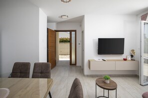 A modern living room with a flat-screen TV, a dining area with a wooden table, and a small round table with a plant. - Family Villa Korina in Peroj (Peroj)