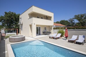 Ein zweistöckiges Gebäude mit Swimmingpool, Sitzgelegenheiten im Freien und Grillplatz.