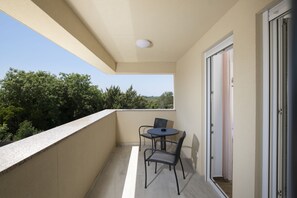 Ein Balkon mit Tisch und Stühlen, einer Tür und Blick auf Bäume.