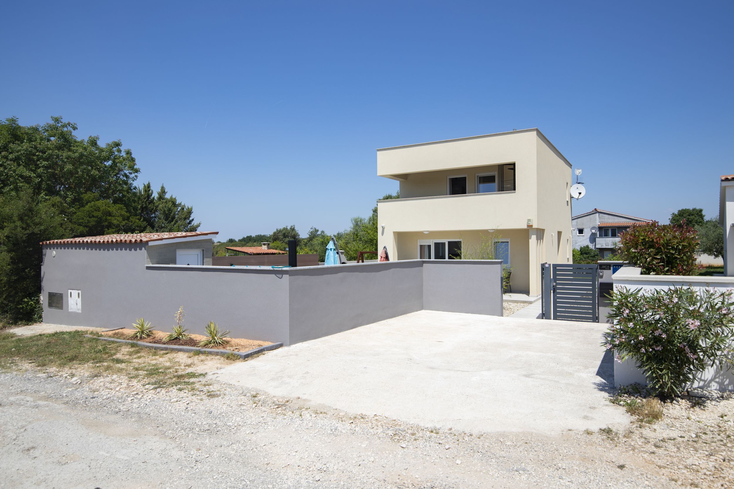 A modern two-story house with a flat roof, a concrete driveway, and a gated entrance.