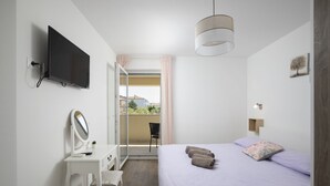 Ein Schlafzimmer mit Bett, Schreibtisch mit Spiegel, Fernseher und Blick ins Freie.
