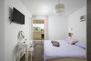 A bedroom with a bed, a desk with a mirror, a television mounted on the wall, and a view of the outside. - Family Villa Korina in Peroj (Peroj)