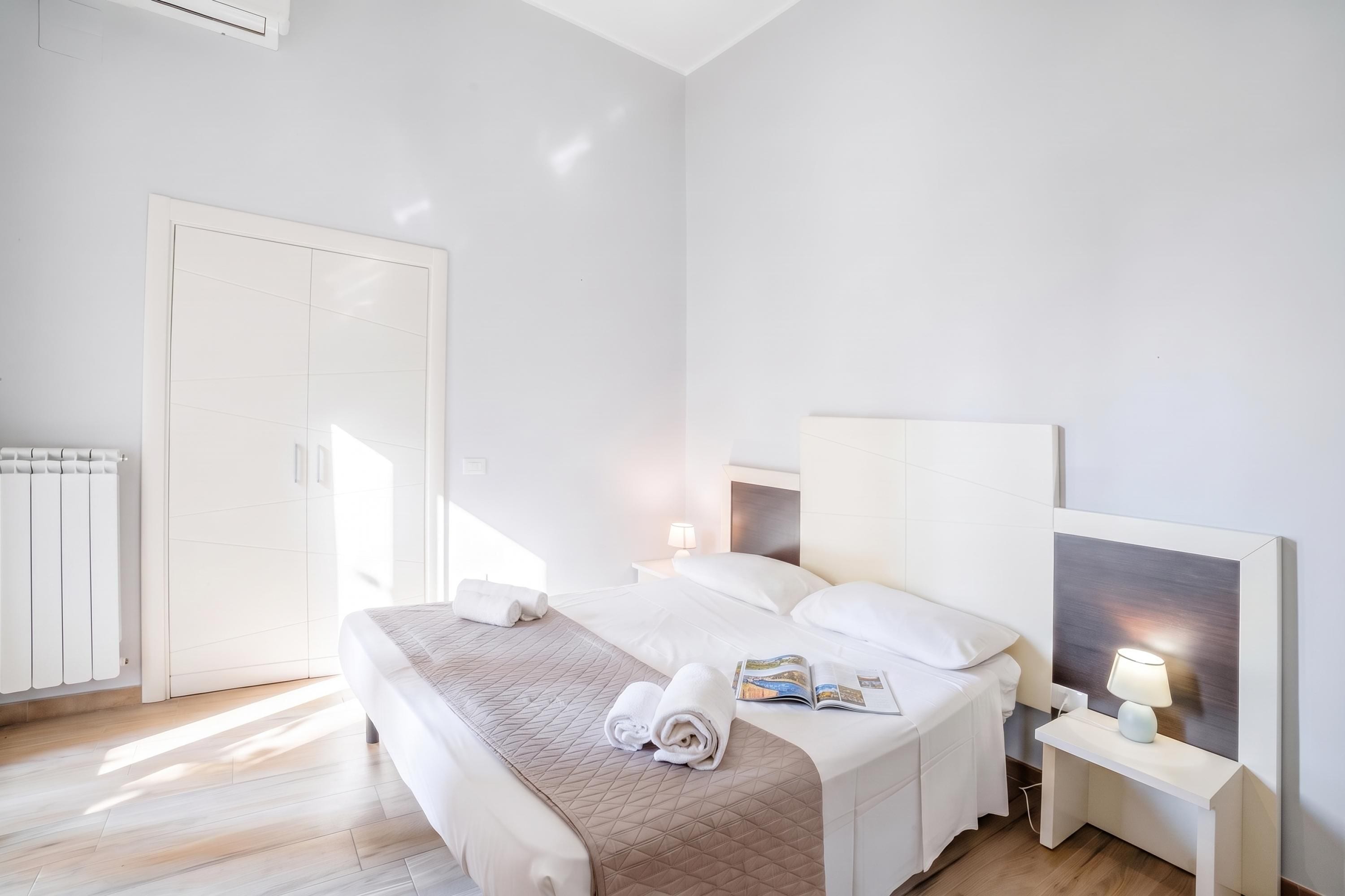 A hotel room with a bed, bedside tables, a nightstand, a radiator, and a door.