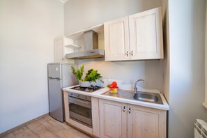 Cocina compacta con refrigerador, estufa, horno y pileta con grifo moderno.