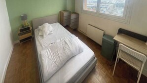 Makuuhuoneessa on sänky, työpöytä, tuoli, lipasto ja ikkuna, josta on näkymä kaupunkiin.