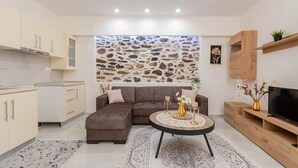 A modern living room with a sectional sofa, a round coffee table, a flat-screen TV, and a stone wall. - Paradise House (Sithonia)