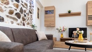 A modern living room with a stone wall, a grey sofa, a TV, and decorative vases. - Paradise House (Sithonia)
