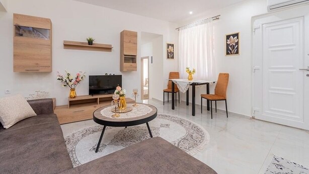 A modern living room with a sofa, TV, dining table, chairs, and a small coffee table. - Paradise House (Sithonia)