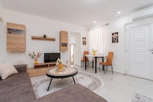 Una sala de estar moderna con un sofá, televisión, mesa de comedor, sillas y una pequeña mesa de centro.