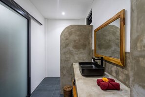 A bathroom with a modern design, featuring a large mirror, a black sink, and a towel with a flower. - Villa Alexine (Seminyak)