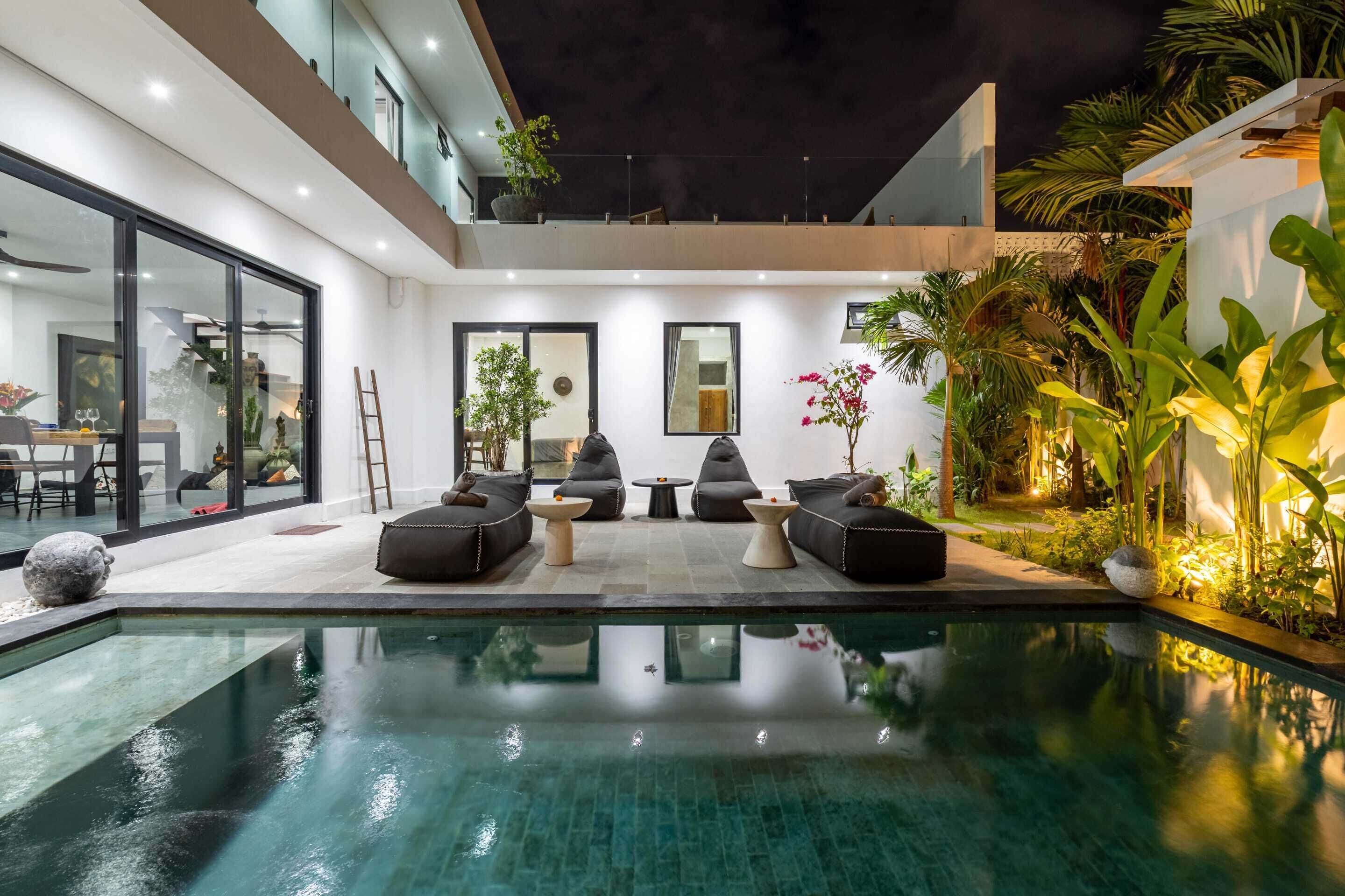 Ein moderner Poolbereich im Freien mit einer verglasten Terrasse, schwarzen Liegestühlen und verschiedenen Pflanzen.