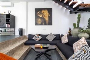 Ein modernes Wohnzimmer mit einer schwarzen Couch, gemusterten Kissen, einem Couchtisch und einem großen Elefantenbild an der Wand.