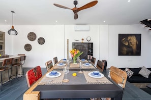 A dining area with a long table, chairs, a ceiling fan, wall decorations, and a sofa. - Villa Alexine (Seminyak)