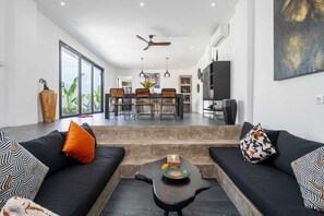 A modern living room with black sofas, a coffee table, and a dining area in the background. - Villa Alexine (Seminyak)