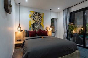 A modern bedroom with a large bed, two bedside lamps, a painting on the wall, and a view of the outdoors. - Villa Alexine (Seminyak)