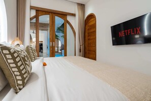 A hotel room with a bed, a TV displaying 'NETFLIX,' and a wooden door. - Villa Atlas (Legian)