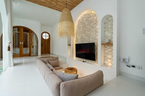 Ein modernes Wohnzimmer mit einer großen Couch, einem an einer Steinwand montierten Fernseher und einer Hängeleuchte.