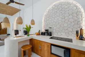 A modern kitchen with a stone backsplash, wooden cabinets, and a built-in dishwasher. - Villa Atlas (Legian)