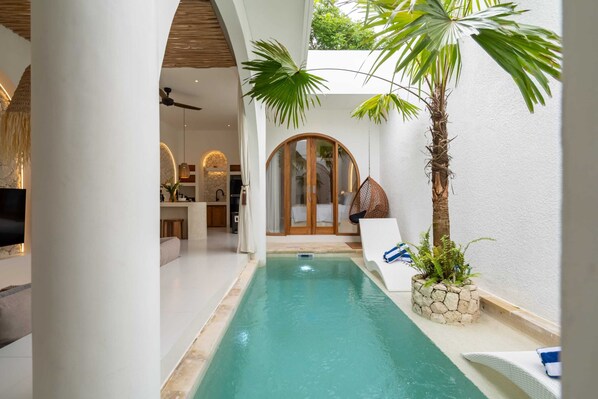 A pool area with a clear view of the pool, a palm tree, and a stone planter. - Villa Atlas (Legian)